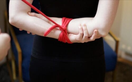 Arms tied in a box tie behind her back for rope bondage purposes